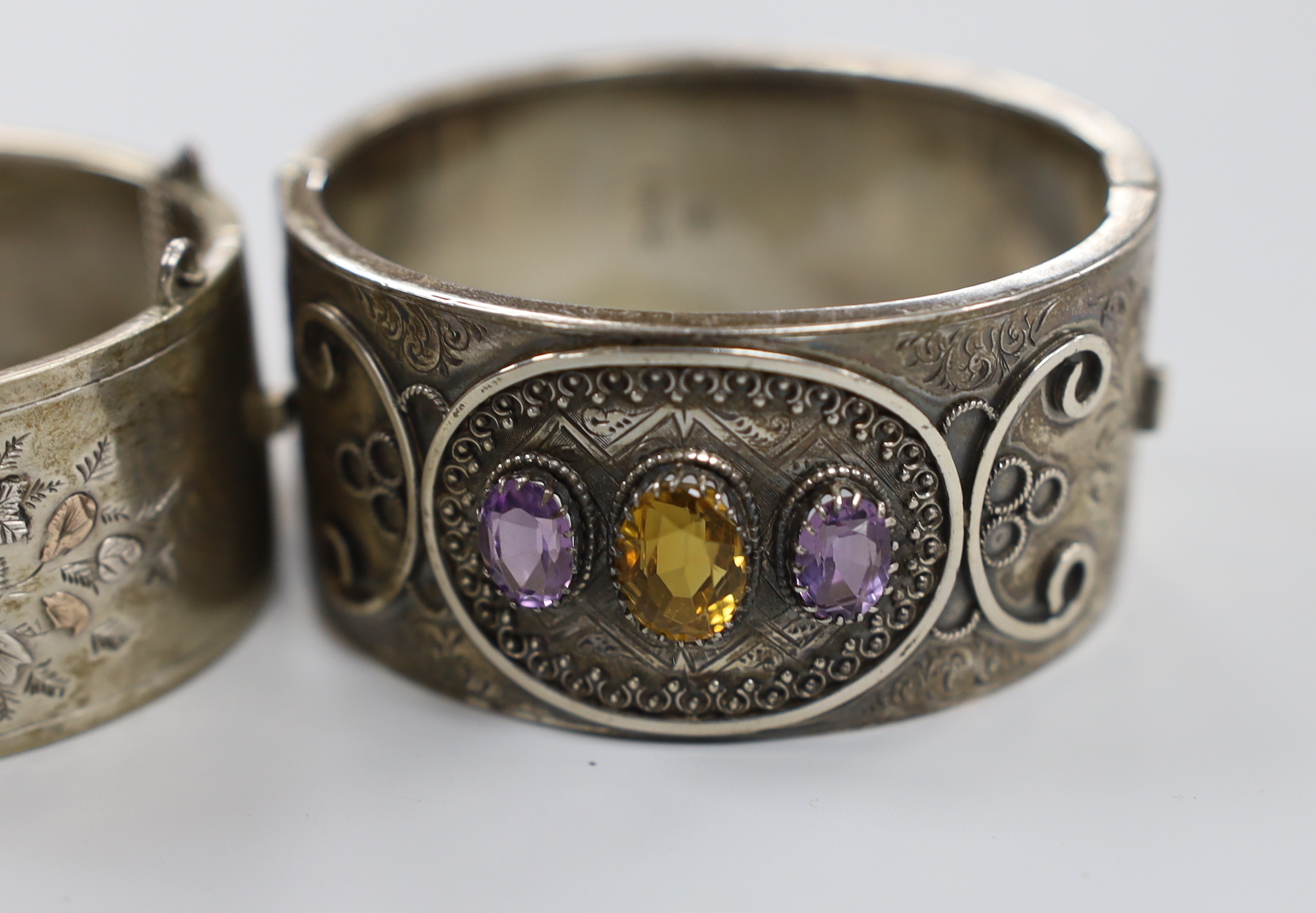 A late Victorian silver and three stone amethyst and citrine set hinged bangle and a later white metal bangle.